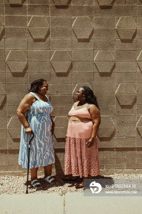 2 plus size African American women talk and laugh standing against a wall