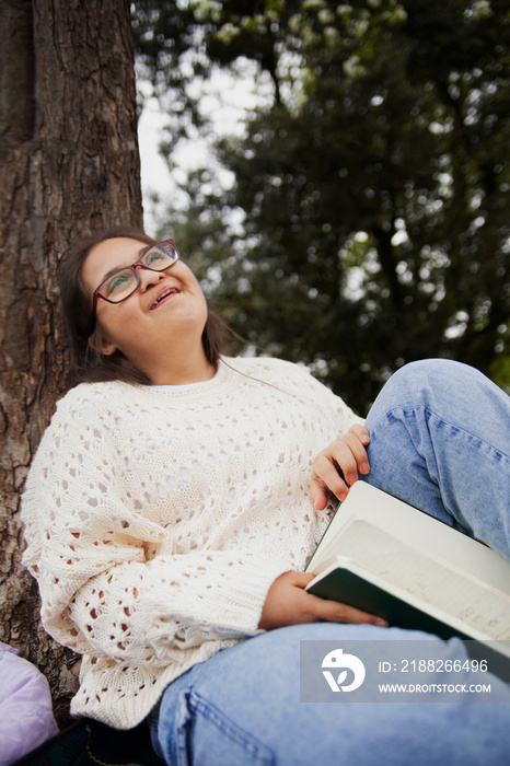 Happy curvy woman with Down syndrome reading in the park