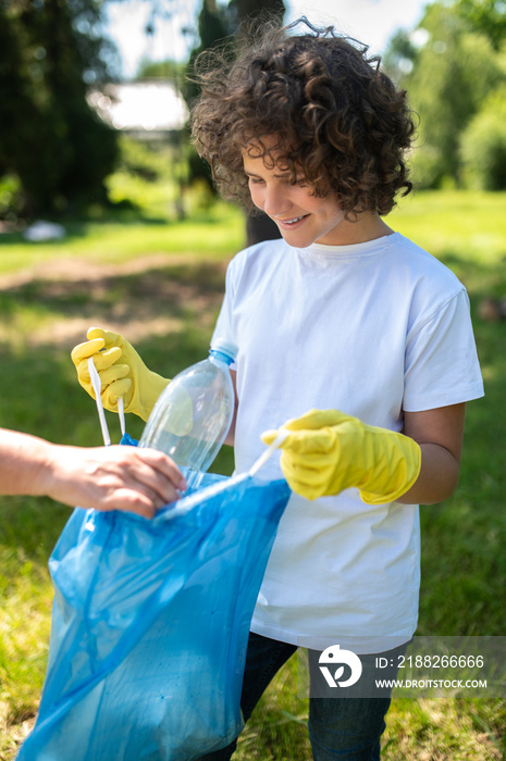 Someone helping a curly-haired teen to gather garbage