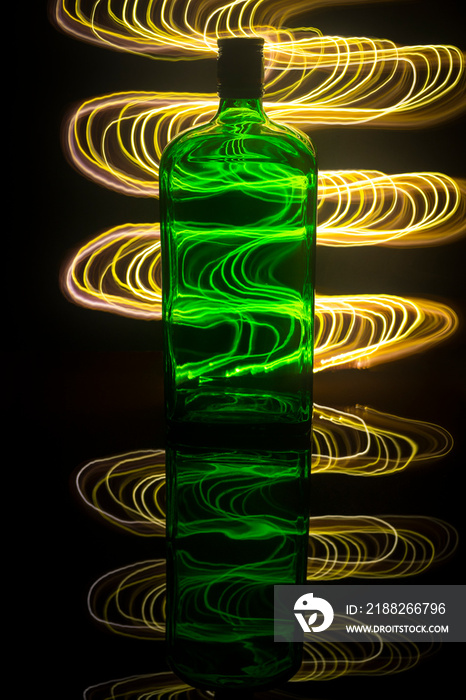 A green bottle on the background which is illuminated with light painting.