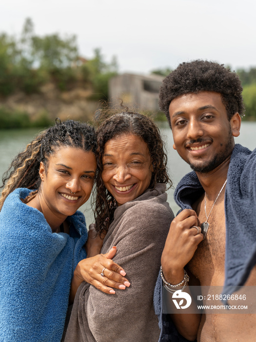 Portrait of smiling friends wrapped in towels by lake