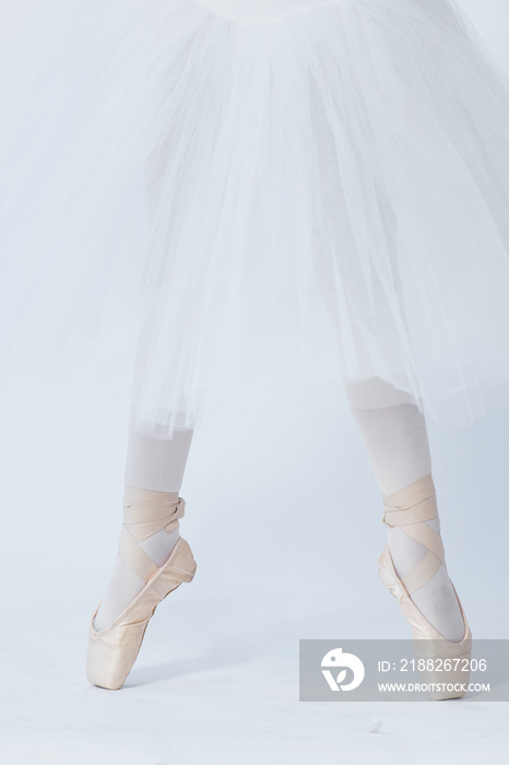 A girl stands on outstretched legs, shod in pointe shoes. A child in a white dress for dancing and white tights. Feet in pointe. Exercises in the ballet school. Ballet classes. White background.