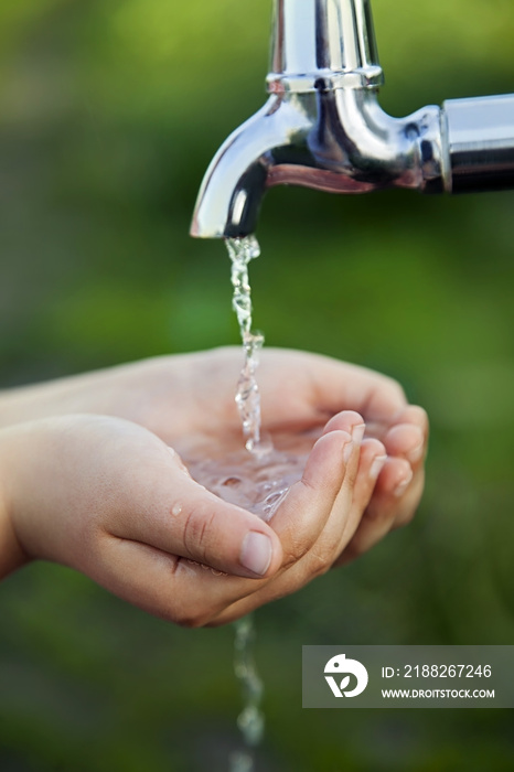 boy washes his hand under the faucet in garden