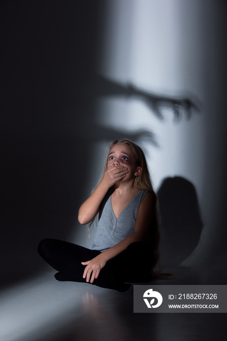 Sad and frightened little girl with bloodshot, bruised eyes crying scared of shadow on the wall. Concept of child violence, domestic abuse. Sad, depressed being victim of parents and their agression.