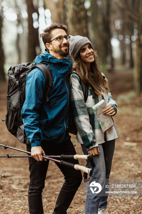 Smiling young european couple tourists in jackets with backpack, trekking sticks and map walk