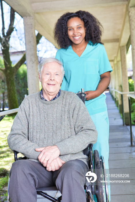Aged senior man on the wheelchair assisted by african nurse in the garden patio