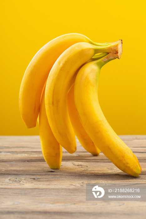 bunch of bananas on  wooden table on yellow background