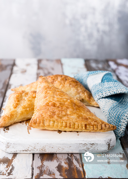 Puff pastry triangles filled with apples, dutch appelflappen on old cutting board. Homemade food concept with copy space.