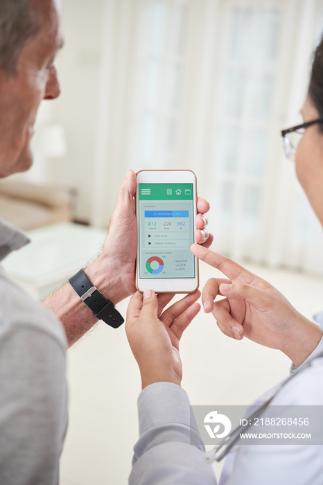 Crop doctor holding smartphone and showing application for healthy lifestyle during home visit