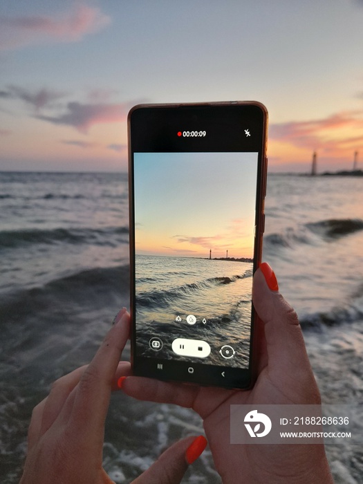 Taking photo of sea waves on smartphone. Landscape of the evening sea filmed on a mobile phone.