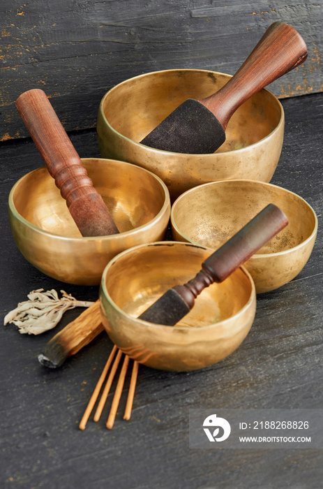 Tibetan singing bowls with palo santo, white sage and aroma sticks on the dark background. Nepal music instruments for meditation, relaxation after yoga practice and healing massage