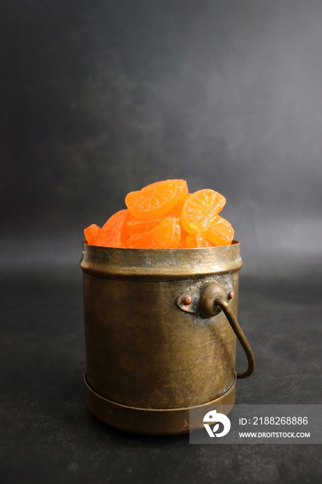 Orange candy. Indian Vintage style boiled sugar confectionery Orange flavored candy or chocolate. Old school nostalgia snacks of 90s kids. Served in a brass container with papercrafts. Copy space.