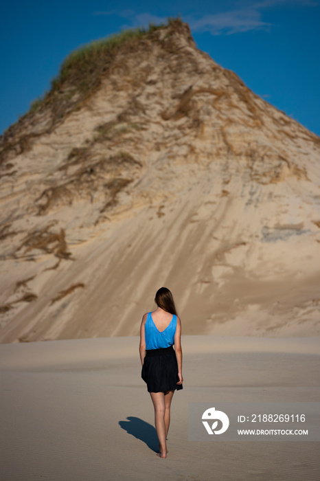 young long-haired woman with huge dunes and sandy hills in the background; woman lost in the desert