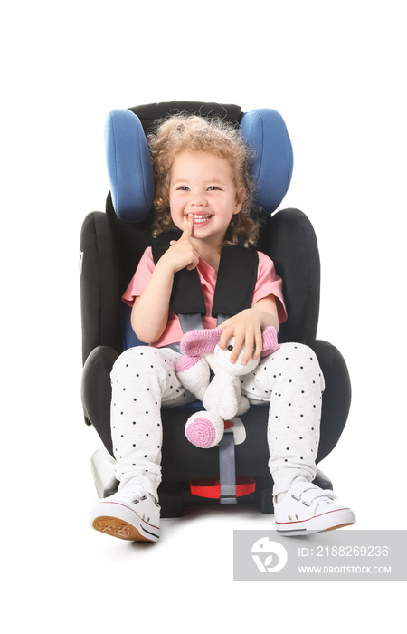 Cute little girl with toy buckled in car safety seat on white background