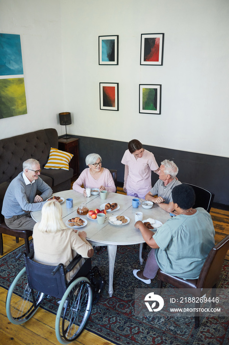 Vertical high angle view at diverse group of senior people enjoying breakfast at dining table in nursing home, copy space