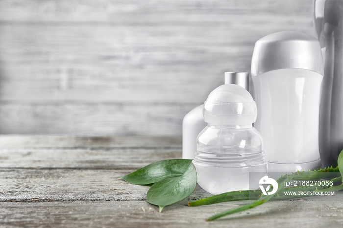 Different deodorants and leaves on wooden background