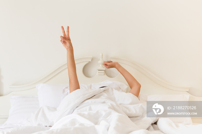 Woman in bed under the blanket stretching hand after waking up.