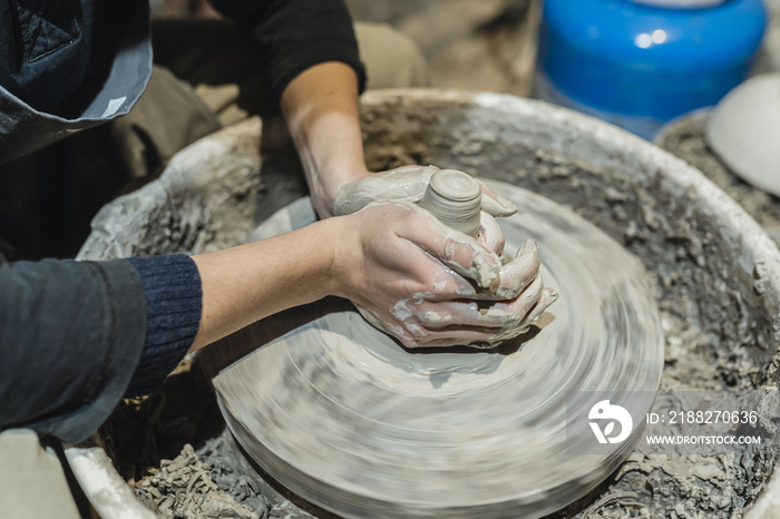 potter’s female hands, soiled in clay, form clay lump on potter’s wheel. Craft clay pottery, hobby folk art