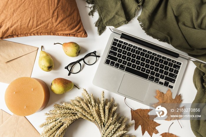 Home office table desk workspace with laptop, glasses, wreath of wheat straw, dry autumn leaves, pears, blanket, pillow, envelops. Fall autumn concept. Flat lay.