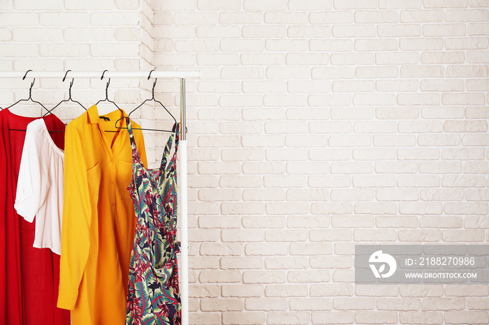 Women’s hip clothing store interior concept. Row of different colorful female clothes hanging on rack in hipster fashion show room in shopping mall. White brick wall background. Copy space.