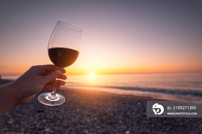 Person holding glass of red wine during watching sunset and enjoying sea holiday