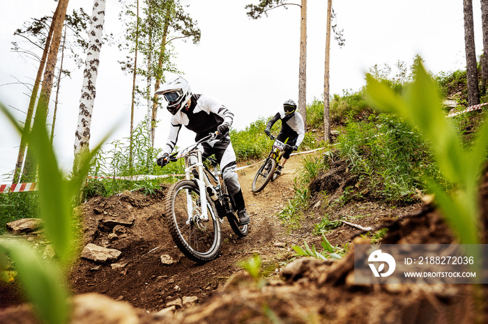 two downhill mountain biker on forest trail. rides competition DH