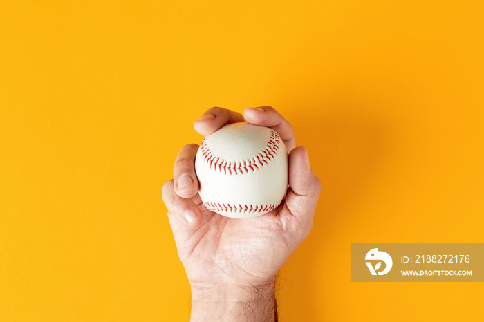 Male hand holds a baseball ball on yellow background.