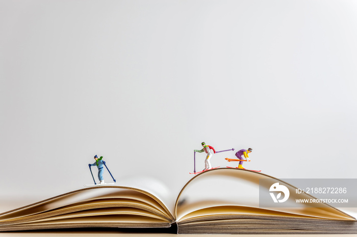 Miniature skiers sliding down the open book