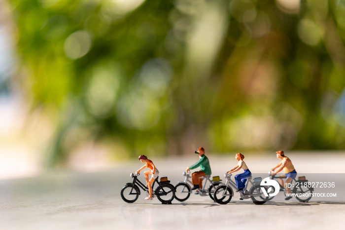 Miniature people  ride a  bicycle outdoors with green bokeh background