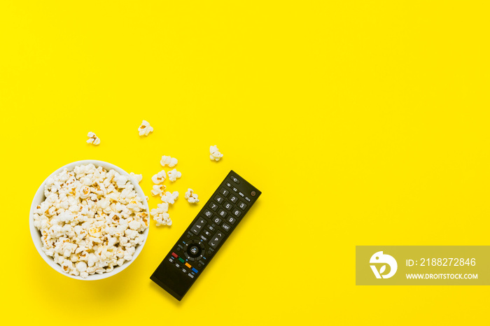 A bowl of popcorn and TV remote on a yellow background. The concept of watching TV, film, TV series, sports, shows. Flat lay, top view.
