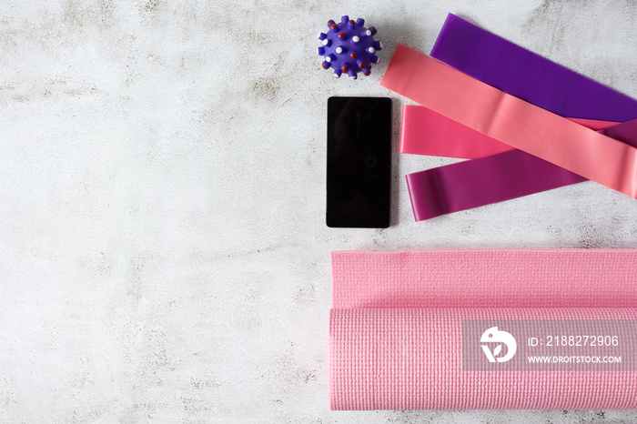 Fitness rubber bands, yoga mat, massage ball and smartphone on grey concrete floor.