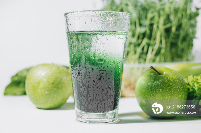 chlorophyll in a glass of water on a white background near are various fresh vegetables fruits and roots with lettuce and spinach