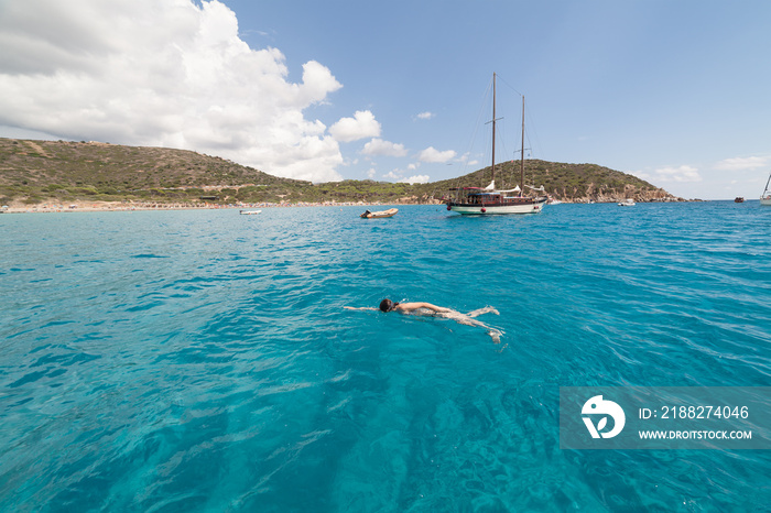 Seascape with swimming woman and some boats turquoise sea of Mari Pintau - Sardinia - Italy