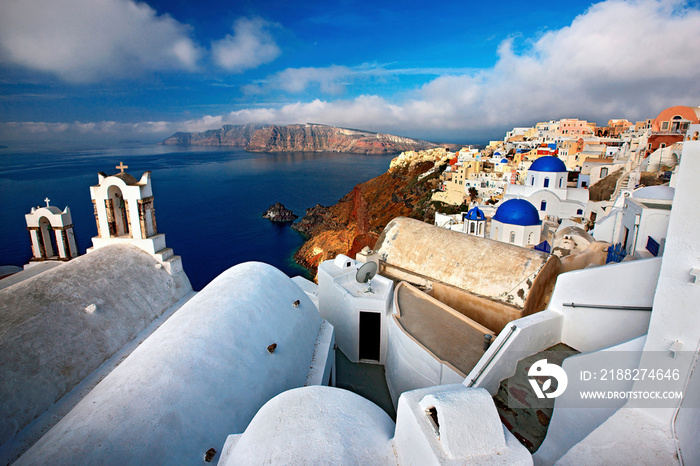 Santorini or Thira or Thera island, wide angle view of picturesque Oia village, hanging over the caldera. In the background, Thirasia island