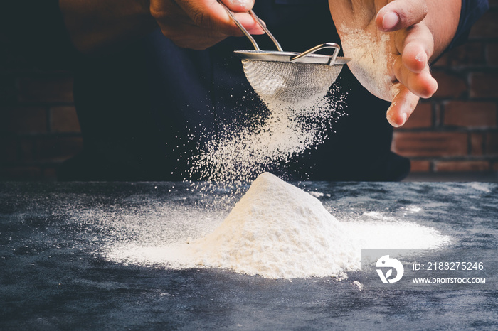 Chef sifting flour on black table