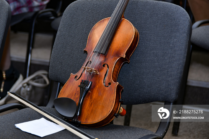 A violin with a bow and notes stands on a chair in the middle of an empty concert hall.