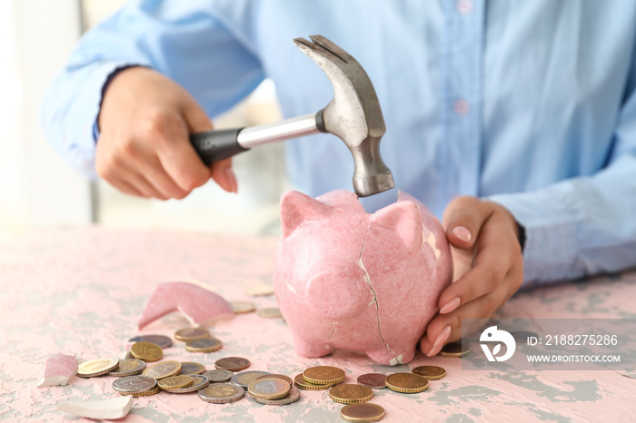 Woman breaking piggy bank at table