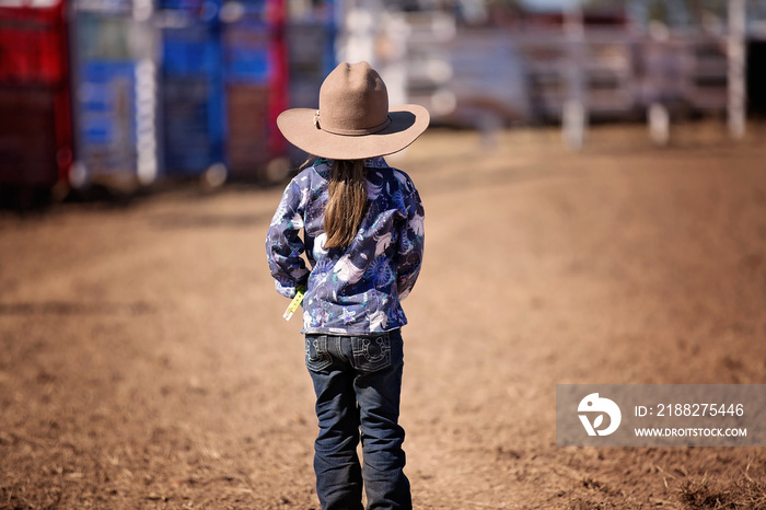 Little Cowgirl Stands In The Dust Watching A Country Rodeo