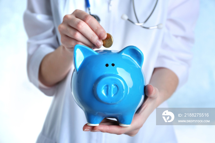 Female doctor putting coin into piggy bank, close up. Concept of medical insurance