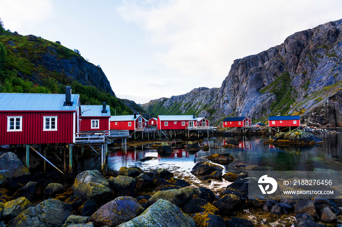 Nusfjord harbor with colorful red fishing houses and sailing boat in a peaceful evening, Lofoten Islands, Norway