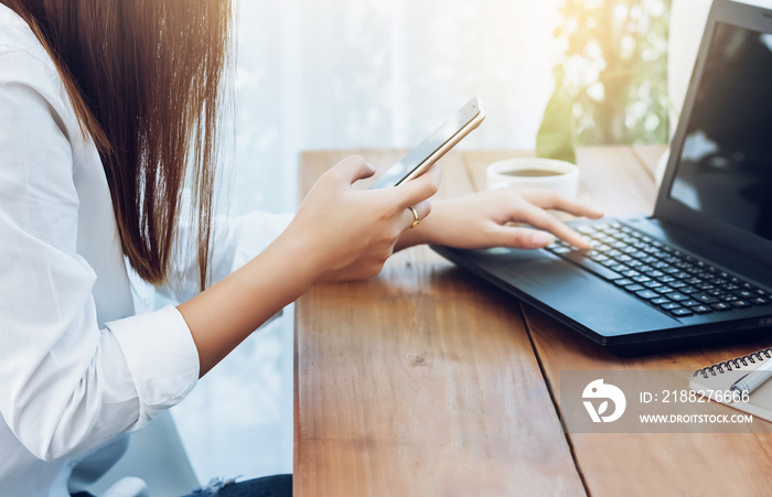 Closeup asian woman using smartphone and laptop working online on wooden table