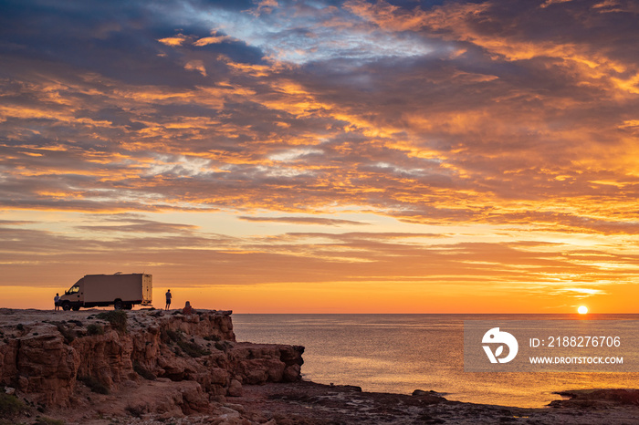 sunset / sunrise at rocky cliff with travel trailer above the sea. Dramatic and calm cloudy sky with sun beams