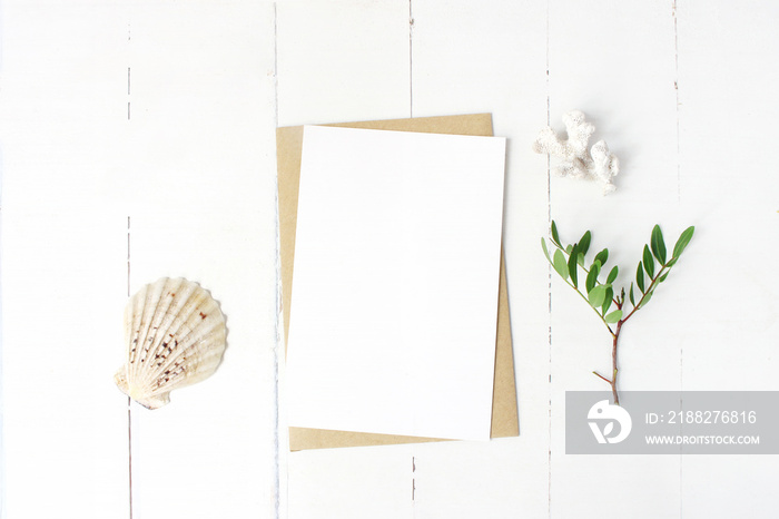 Summer marine stationery, desktop mock-up scene. Blank greeting card, craft envelope, seashell, coral and lentisk branch. Old white wooden table background. Flat lay, top view.