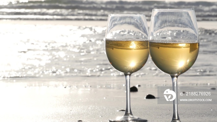 Two wineglasses on sandy ocean beach. Couple of glasses and pebbles, white wine for romantic date near sea water. Cozy beachfront sunset near tide waves. Seamless looped cinemagraph. California, USA.