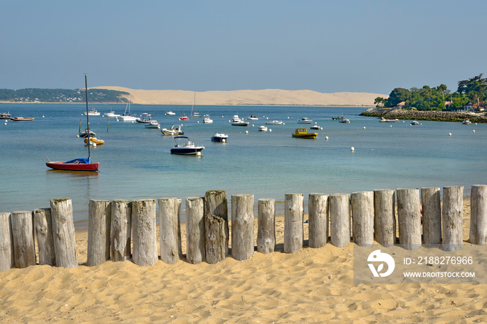 Beach with wooden trunks protecting the dunes of Cap-Ferret, boats and the Pilat dune in the background. Commune in the Gironde department in southwestern France
