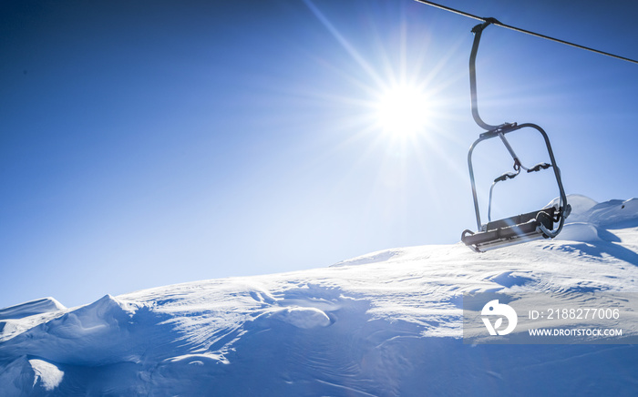 Ski lift seats high in the mountains. Winter elevator mountains panorama with sun and blue sky in background. Copy space for text.