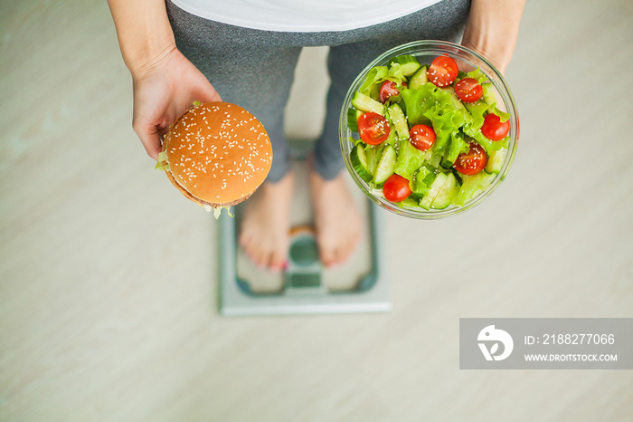 Dieting concept, beautiful young woman choosing between healthy food and junk food