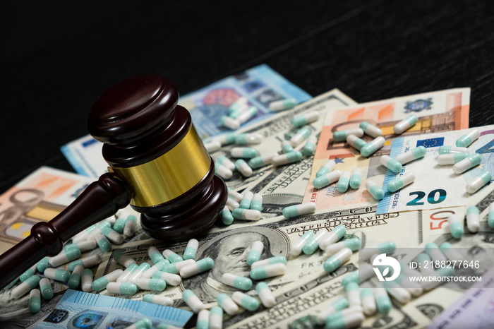 Wood judge’s gavel and scattered colorful drugs on the dollar and euro cash background