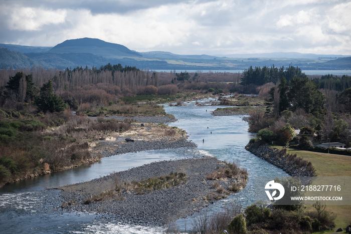 Elevated view of the Tongariro River with four fly fishermen wading, and fishing for trout. Lake Taupo and mountains in the background.