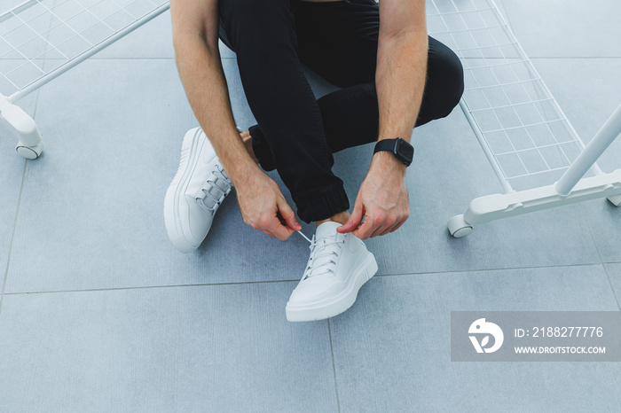 Men’s in white leather casual lace-up sneakers and black trousers against a gray tile background